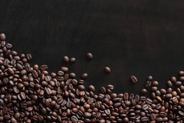 stock image Roasted coffee beans on a wooden dark table, top view. Background of fragrant brown coffee beans scattered over the surface. copy space. Place for text