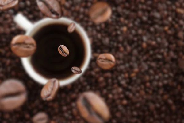 Coffee beans fall into a cup of coffee. White cup with coffee on the background of coffee beans. Energy drink, caffeine. Selective focus