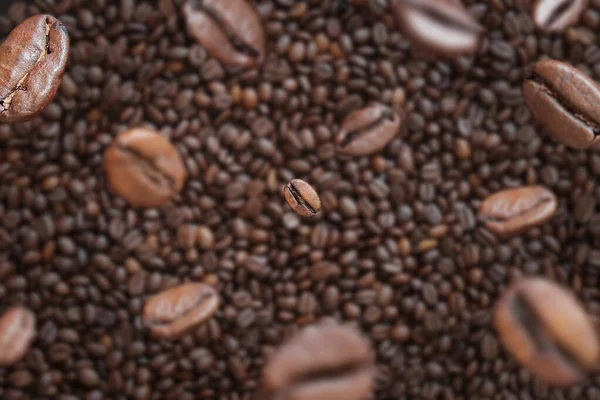 Coffee beans fall into a pile, selective focus. Pile of halves of dark brown coffee beans, copy space