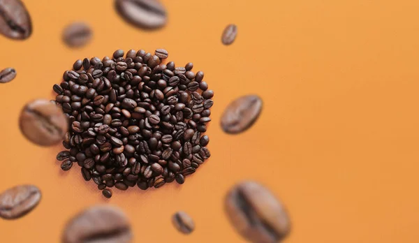 Coffee beans fall into a pile, selective focus. Pile of halves of dark brown coffee beans, copy space. Orange background