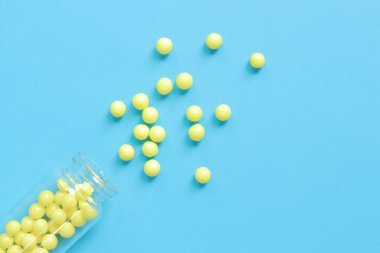 Sarı haplar mavi arka plandaki cam şişeden döküldü. Ascorbic asit, üst görüş, kopyalama alanı. Sağlık, tıbbi ilaçlar ve beslenme malzemeleri. C vitamini