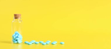 Sarı arka planda cam şişedeki mavi haplar. Vitaminler şişenin yanına saçılmış, yan görüş. Sağlık hizmetleri, ağrı kesiciler, ilaç hapları ve diyet takviyeleri