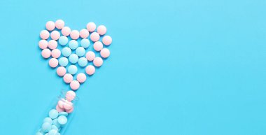 Pembe ve mavi haplı cam şişe. Mavi arka planda vitaminlerle kaplanmış kalp, üst manzara. Sağlık sigortası, tıbbi ilaçlar ve diyet takviyeleri. Eczacılık ilaçları.