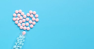 Pembe ve mavi haplı cam şişe. Mavi arka planda vitaminlerle kaplanmış kalp, üst manzara. Sağlık sigortası, tıbbi ilaçlar ve diyet takviyeleri. Eczacılık ilaçları.
