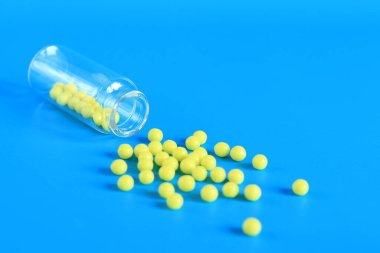 Sarı haplar mavi arka plandaki cam şişeden dökülür. Ascorbic asit, uzayı kopyala. Sağlık, tıbbi ilaçlar ve besin takviyeleri. C vitamini