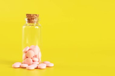 Sarı arka plandaki cam şişeden pembe haplar dökülüyor. Vitamin kompleksi, yan görüş, kopyalama alanı. Sağlık sigortası, ilaç ve beslenme takviyeleri.