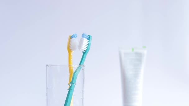 女性の手がガラスに歯ブラシをかける 白い背景にガラスビーカーの歯ブラシ 口腔衛生について 歯のクリーニング 日々の衛生のコンセプト — ストック動画