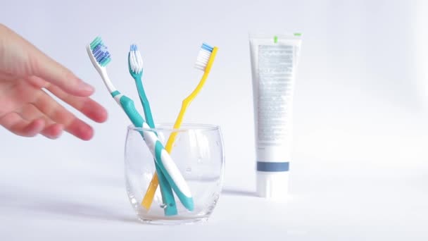 女性の手は歯ブラシを取ります 白い背景にガラスビーカーの歯ブラシ 口腔衛生について 歯のクリーニング 日々の衛生のコンセプト — ストック動画