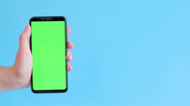Elinde akıllı telefondan krom anahtar modeli var. Uygulama veya web sitesi tasarımı için kopya alanı gösteriliyor. Bir kadın elinde mavi arka planda boş yeşil ekranlı akıllı bir telefon tutuyor.