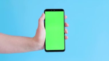 Elinde akıllı telefondan krom anahtar modeli var. Uygulama veya web sitesi tasarımı için kopya alanı gösteriliyor. Bir kadın elinde mavi arka planda boş yeşil ekranlı akıllı bir telefon tutuyor.
