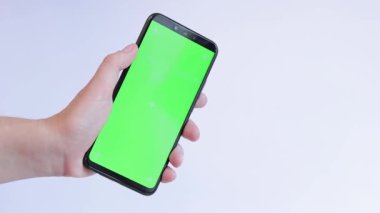 Beyaz arka planda yeşil ekranlı bir telefon. Uygulama veya web sitesi tasarımı için kopya alanı gösteriliyor. Bir kadın elinde açık yeşil ekranlı bir akıllı telefon tutuyor.
