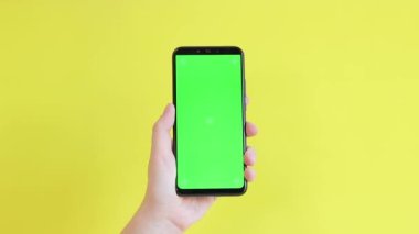 Elinde akıllı telefondan krom anahtar modeli var. Uygulama veya web sitesi tasarımı için kopya alanı gösteriliyor. Sarı arka planda boş yeşil ekranlı akıllı telefon tutan bir kadın var.