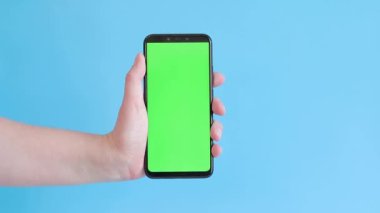 Elinde akıllı telefondan krom anahtar modeli var. Uygulama veya web sitesi tasarımı için kopya alanı gösteriliyor. Bir kadın elinde mavi arka planda boş yeşil ekranlı akıllı bir telefon tutuyor.
