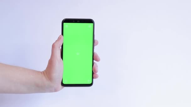 白い背景に手のひらに緑色のスクリーンが付いている電話 アプリやウェブサイトのデザインのコピースペースを展示します 女性が空白の緑の画面でスマートフォンを保持しています — ストック動画