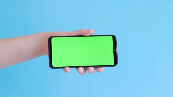 スマートフォンのクロマキーモックアップ アプリやウェブサイトのデザインのコピースペースを展示します 女性が青い背景に白い緑色の画面を持つスマートフォンを保持しています — ストック動画