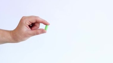 Beyaz arka planda vitaminler. El, iki parmaklı yeşil bir hap tutuyor. Tıp ve sağlık kavramı. Vitaminler ve besin takviyeleri