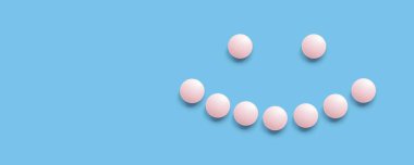 Mavi arka planda pembe haplarla kaplı gülümseyen yüz, üst manzara. Sağlık, tıbbi ilaçlar ve besin takviyeleri. Eczacılık.