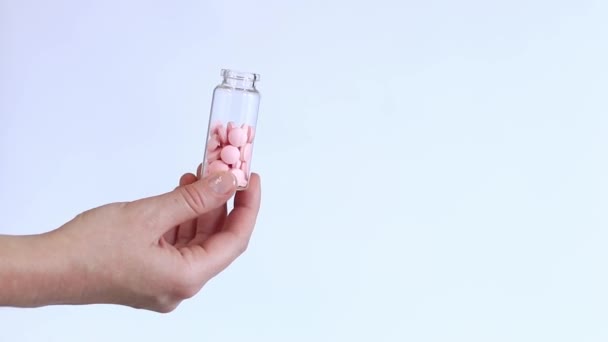 ガラス瓶の中のピンクの錠剤 白い背景に女性の手のビタミン ビタミンと栄養補助食品のクローズアップ — ストック動画