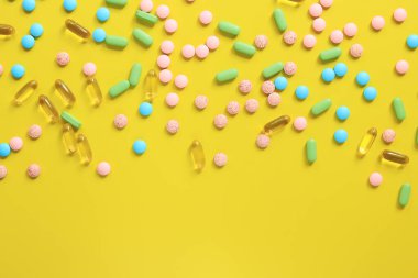 Sarı arka planda farklı renkte vitaminler. Dağınık parlak hapların en üst görüntüsü. İlaç sanayisi. Sağlık ve ilaç. Eczane ürünü. Mesaj için yeri olan pankart. Boşluğu kopyala