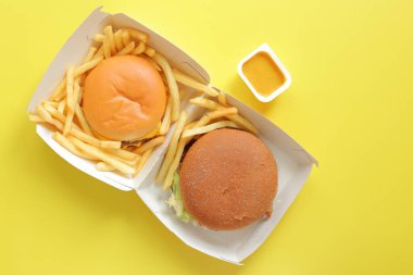 Sarı arka planda, üzerinde hamburger ve patates kızartması olan karton kutuyu aç. Fast food restoranı.