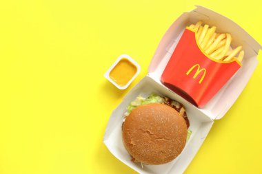 Kyiv, Ukrayna - 10 Ağustos 2023: Sığır etli çavdar burger, orta ölçekli patates kızartması ve hardal, üst görünüm. Parlak sarı arka plan. McDonald 's Corporation dünyanın en büyük fast food restoranıdır.