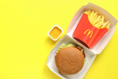 Kyiv, Ukraine - August 10, 2023: Rye burger with beef, medium portion of french fries and mustard, top view. Bright yellow background. McDonald's Corporation is the world's largest fast food restauran clipart