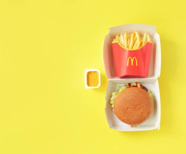 Kyiv, Ukrayna - 10 Ağustos 2023: Sığır etli çavdar burger, orta ölçekli patates kızartması ve hardal, üst görünüm. Parlak sarı arka plan. McDonald 's Corporation dünyanın en büyük fast food restoranıdır.