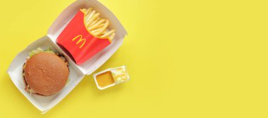 Kyiv, Ukrayna - 10 Ağustos 2023: Sığır etli çavdar burger, orta ölçekli patates kızartması ve hardal, üst görünüm. Parlak sarı arka plan. McDonald 's Corporation dünyanın en büyük fast food restoranıdır.