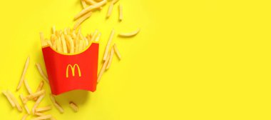 Kyiv, Ukrayna - 10 Ağustos 2023: Sarı arka planda patates kızartması. McDonald 's Corporation dünyanın en büyük fast food restoranıdır. Kağıt ambalajlı patatesler ve yanında düz bir şekilde yatıyordu.