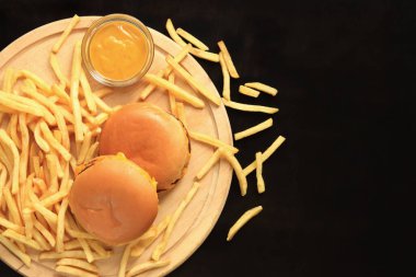 Kesme tahtasında çizburger ve patates kızartması, üst manzara, koyu ahşap arka plan. Fast food. Hamburger, patates kızartması ve hardal.