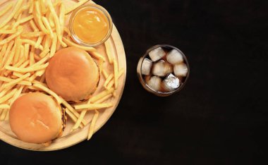 Kesme tahtasında çizburger ve patates kızartması, buzlu kola, üst manzara, koyu ahşap arka plan. Fast food. Hamburger, patates kızartması ve hardal.