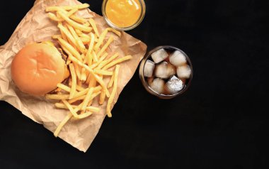 Kahverengi kağıt üzerinde çizburger ve patates kızartması ve ahşap masa, üst manzara. Hamburger, patates kızartması, buzlu kola ve hardal. Fast food