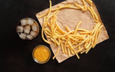 Fast food. Kahverengi kağıtta patates kızartması, buzlu ve hardallı kola, ahşap masa, üst manzara. Fast food restoranı. Boş yer