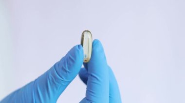 Mavi lateks eldivenli bir elin içinde balık yağı kapsülü var. Tıp ve sağlık hizmetleri kavramı, farmakoloji. Doktor vitamin gösteriyor. Vitaminler ve besin takviyeleri. Omega-3 balık yağı kapsülü