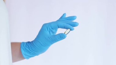Mavi lateks eldivenli bir elin içinde balık yağı kapsülü var. Tıp ve sağlık hizmetleri kavramı, farmakoloji. Doktor vitamin gösteriyor. Vitaminler ve besin takviyeleri. Omega-3 balık yağı kapsülü