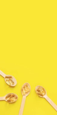 Omega 3. Sarı arka planda, ahşap kaşıklarda balık yağı bulunan altın kapsüller, üst manzara. İlaç sanayisi. Sağlık ve ilaç. Eczane ürünü