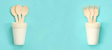 Tek kullanımlık tahta kaşıklar ve çatallar beyaz kağıt bardaklarda, üst manzara. Çevre dostu tek kullanımlık mutfak aletleri mavi arka planda, kopyalama alanı. Düz plan. Ekolojik yemek kavramı