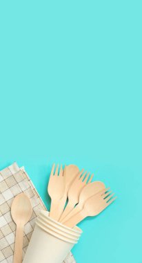 Kağıt bardakta tek kullanımlık tahta çatallar ve kaşıklar, üst manzara. Çevre dostu tek kullanımlık mutfak aletleri mavi arka planda, kopyalama alanı. Düz yatıyordu. Sıfır atık