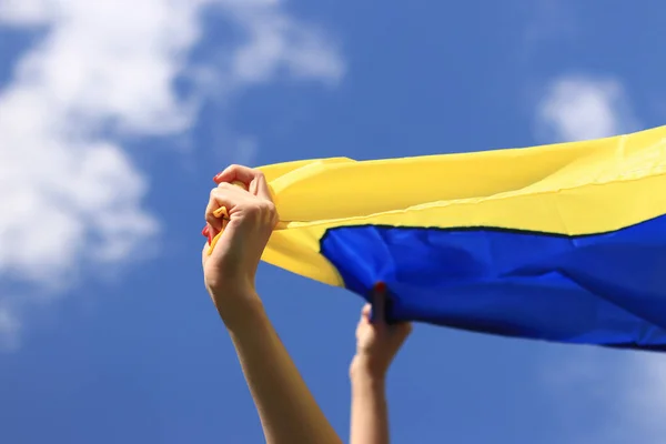 Yellow and blue flag of Ukraine in the woman's hands. Fluttering blue and yellow flag of Ukraine against sky background. Ukrainian flag is a symbol of independence