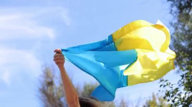 Gökyüzüne karşı Ukrayna bayrağı taşıyan kadın elleri. Elinde sarı-mavi bayrak olan bir kız. Bayrak rüzgarda dalgalanıyor. Vatanseverlik