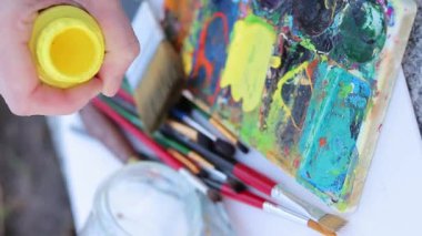 Paletin üzerine boya döküyorum. Çizmeye hazırlanıyorum. Kavanozdan sarı akrilik boya dökülüyor, yakın plan. Sanatsal aletler, boyalar, paletler, fırçalar. Dikey video