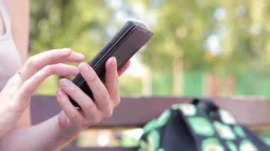 Akıllı telefonlu bir kadın eli, yakın plan. Çevrimiçi iletişim, online alışveriş, sosyal ağlar. Açık hava parkında bir kız telefonunu kullanarak internette bir şey arıyor.