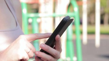 Akıllı telefonlu bir kadın eli, yakın plan. Çevrimiçi iletişim, online alışveriş, sosyal ağlar. Açık hava spor sahasında bir kız telefonunu kullanarak internette bir şeyler arıyor.
