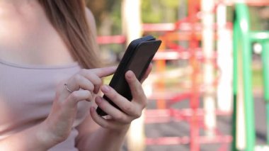 Akıllı telefonlu bir kadın eli, yakın plan. Çevrimiçi iletişim, online alışveriş, sosyal ağlar. Açık hava spor sahasında bir kız telefonunu kullanarak internette bir şeyler arıyor.