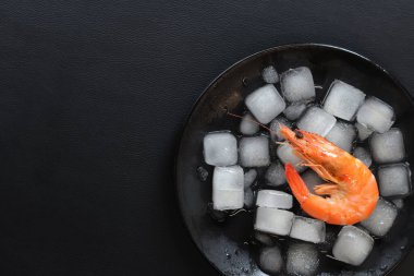 Koyu arkaplanda buzlu, büyük, dondurulmuş karides. Buzlu, siyah bir tabakta kaynamış karides. Ezilmiş buz üzerinde deniz ürünleri. Sağlıklı yeme kavramı