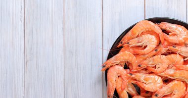 Hafif ahşap arka planda, siyah tabakta kaynamış karides. Taze karides, üst manzara. Deniz ürünleri. Sağlıklı beslenme konsepti. Menü için şablon