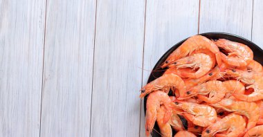 Hafif ahşap arka planda, siyah tabakta kaynamış karides. Taze karides, üst manzara. Deniz ürünleri. Sağlıklı beslenme konsepti. Menü için şablon