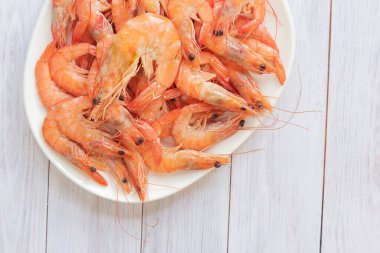 Beyaz tabakta kaynamış karides, ahşap bir arka planda. Taze karides, üst manzara. Deniz ürünleri. Sağlıklı beslenme konsepti. Menü için şablon