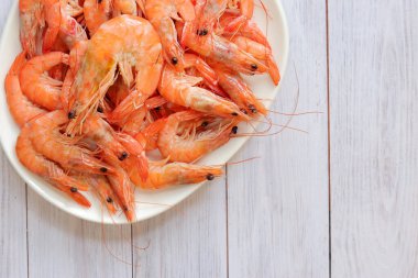 Beyaz tabakta kaynamış karides, ahşap bir arka planda. Taze karides, üst manzara. Deniz ürünleri. Sağlıklı beslenme konsepti. Menü için şablon
