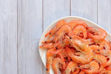 Beyaz tabakta kaynamış karides, ahşap bir arka planda. Taze karides, üst manzara. Deniz ürünleri. Sağlıklı beslenme konsepti. Menü için şablon